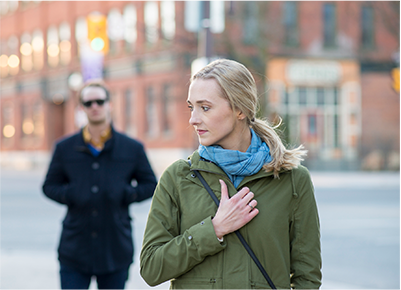 Concerned woman walking on city street with man following behind, representing personal safety awareness.